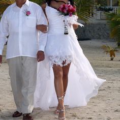 the man and woman are walking down the beach with flowers in their hair, dressed in white