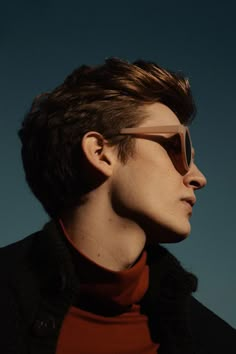 a young man with sunglasses on his face looking off into the distance, against a blue sky