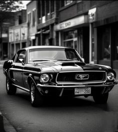 a black and white photo of an old mustang on the street in front of stores