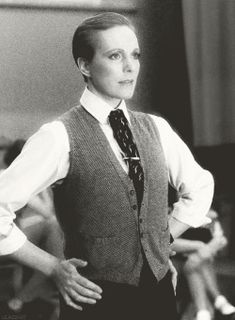 a woman in a vest and tie standing with her hands on her hips