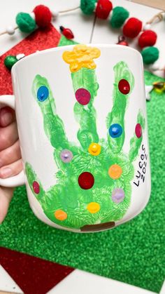 a child's handprinted coffee mug is being held in front of a christmas ornament