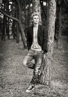 a young man leaning against a tree in the middle of a forest with his hands on his hips