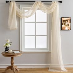 a window with sheer curtains and a small table next to it on a hard wood floor