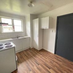 an empty kitchen with wood floors and white cabinets in the corner, next to a stove top oven