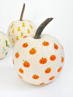 three painted pumpkins sitting next to each other on a white surface with orange and green designs