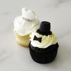 two cupcakes with white frosting and black icing, one has a top hat on it