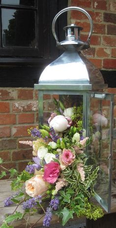 a lantern with flowers in it sitting on a wooden table next to a brick wall