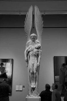 black and white photograph of people looking at art work in an art gallery with two men standing next to the statue