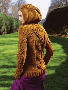 a woman is wearing a sweater with an intricate design on the back and sides, while standing in a grassy area