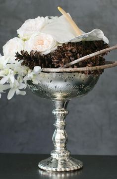 a silver vase filled with white flowers on top of a black table next to a gray wall