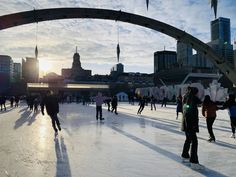 people skating on an ice rink with the sun setting in the background and buildings behind them