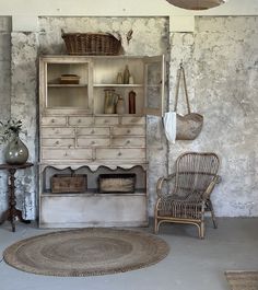 an old fashioned dresser and chair in a room with stone walls, rugs and baskets on the floor