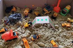 there are many toy trucks and construction vehicles in this sandbox filled with rocks, dirt, and gravel