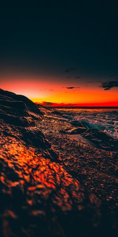 the sun is setting at the beach with waves crashing in front of it and an orange sky