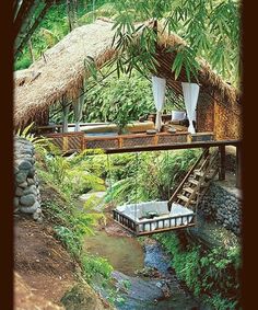 a house in the middle of some trees with a bridge over it and a bed on top