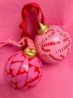 two pink ornaments with red and gold designs on them, one has a ribbon around its neck