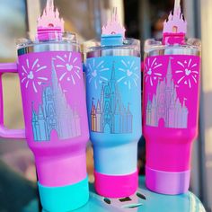 three different colored travel mugs sitting on top of a blue and pink countertop