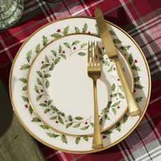 a christmas place setting with holly wreath plates and silverware on a plaid table cloth