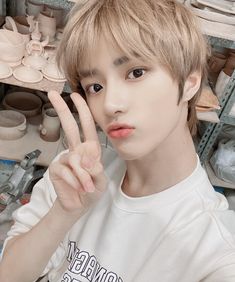 a young man making the v sign with his hand in front of him, surrounded by pottery