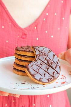 a woman is holding a plate with chocolate covered cookies on it and she is wearing a pink dress