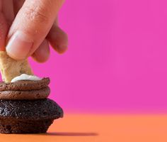 a hand is picking up a piece of bread from a stack of cookies on an orange and pink background