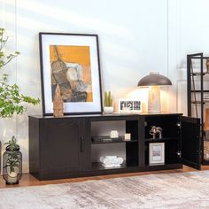 a black entertainment center with pictures on the wall and plants in vases next to it