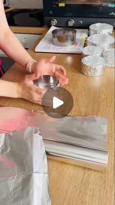 a woman is making something out of aluminum foil on a wooden table in front of a television