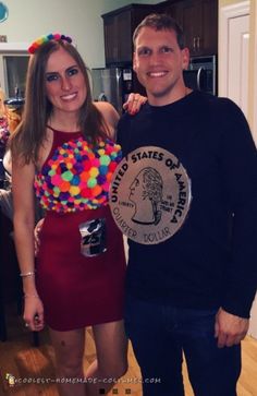 a man and woman standing next to each other in a kitchen holding a plate with pom poms on it