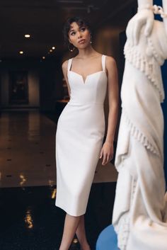 a woman in a white dress standing next to a statue and looking at the camera