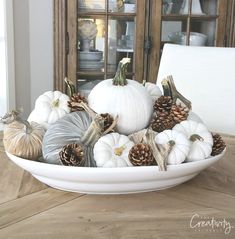 a bowl filled with white pumpkins and pine cones on top of a wooden table