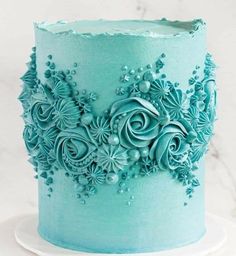 a blue frosted cake with flowers and pearls on the top is sitting on a white plate