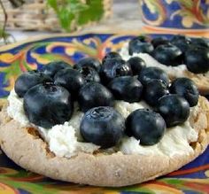 blueberries and cream on top of a bagel with lettuce in the background