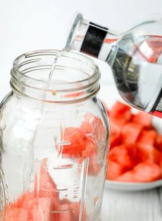 a person pouring water into a mason jar filled with diced red fruit and vegetables