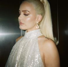 lady with blonde hair and big earrings looking off into the distance while standing in front of a mirror