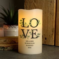 a candle with the word love on it sitting next to some candles and a potted plant