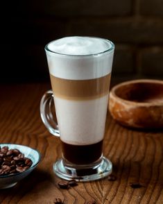 there is a cup of coffee on the table next to a bowl of chocolate beans