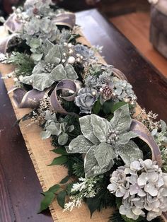 the table is decorated with silver and white flowers, greenery, and ribbon on it