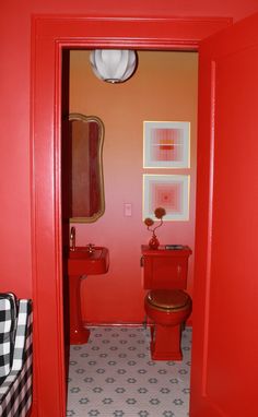 the bathroom is painted bright red and has a toilet, sink, and mirror in it