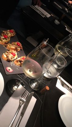 a table topped with plates and glasses filled with wine next to silverware on top of a black counter