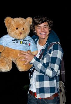 a young man holding a large teddy bear in his right hand and smiling at the camera