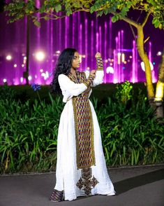 a woman standing in front of a fountain at night with her hand up to the sky