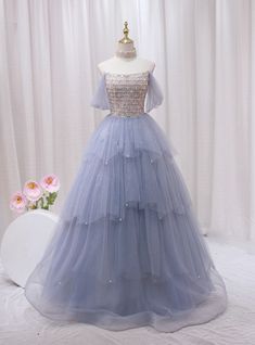 Admire this ethereal blue prom dress, a dream in tulle and sparkle! Fashioned to enchant, this gown features a shimmering, sequined bodice that catches every light, matched with an off-the-shoulder neckline that exudes elegance. The bodice seamlessly transitions into a multi-layered tulle skirt, adorned with delicate sparkles that mimic distant stars in the night sky. Each layer cascades in a gentle flurry, adding volume and a fairy-tale finish to this magnificent dress. Perfect for a prom or any special occasion, this dress guarantees you'll float through the evening with grace and poise. The soft blue hue complements every skin tone, ensuring that you look picture-perfect for every photo opportunity. Fairytale Dress Prom, Ethereal Blue, Gold Tulle, Photo Opportunity, Blue Prom Dress, Prom Dress Plus Size, Layered Tulle Skirt, Marine Uniform, Prom Dresses Two Piece