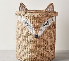 a woven basket with a fox face painted on the front and sides, sitting on a table