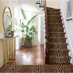 a leopard print rug is on the floor next to a stair case with a mirror and potted plant