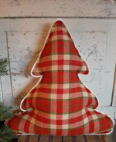 a red and green plaid christmas tree pillow on a wooden shelf next to a potted plant