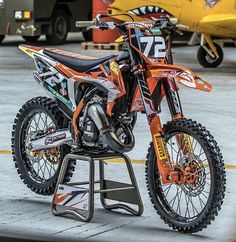 an orange and black dirt bike parked on top of a metal stand in front of a yellow plane