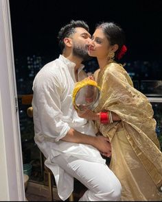 a man and woman kissing each other in front of a window with the city lights behind them