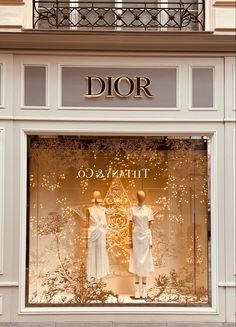 two mannequins in front of a store window with gold and white decorations