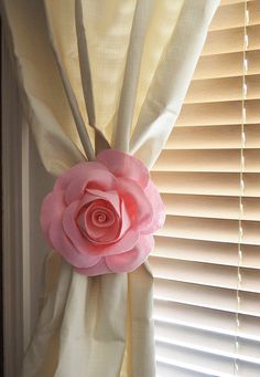 a pink rose is hanging on the curtain in front of a window with white blinds