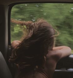 a woman sitting in the passenger seat of a car looking out the window at trees